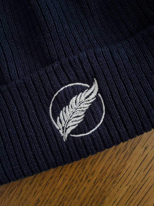 Roho Rafiki® embroidered icon organic cotton beanie. Crafted from 100% organically-sourced Control Union Certified cotton, this lightweight design in a heritage-inspired fine rib is the perfect all-year-round option for casual headwear. Embroidered with the white feather icon logo. Oxford blue.