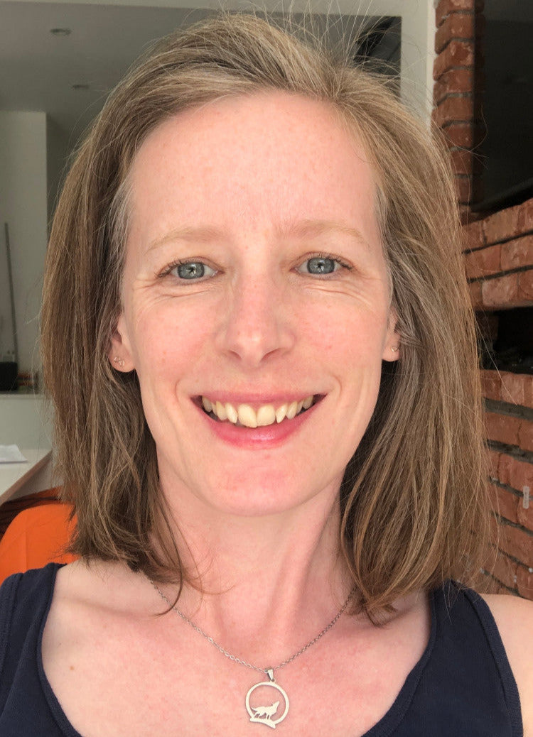 A headshot of Stacey with shoulder-length brown hair, smiling, wearing a dark top, and a necklace.