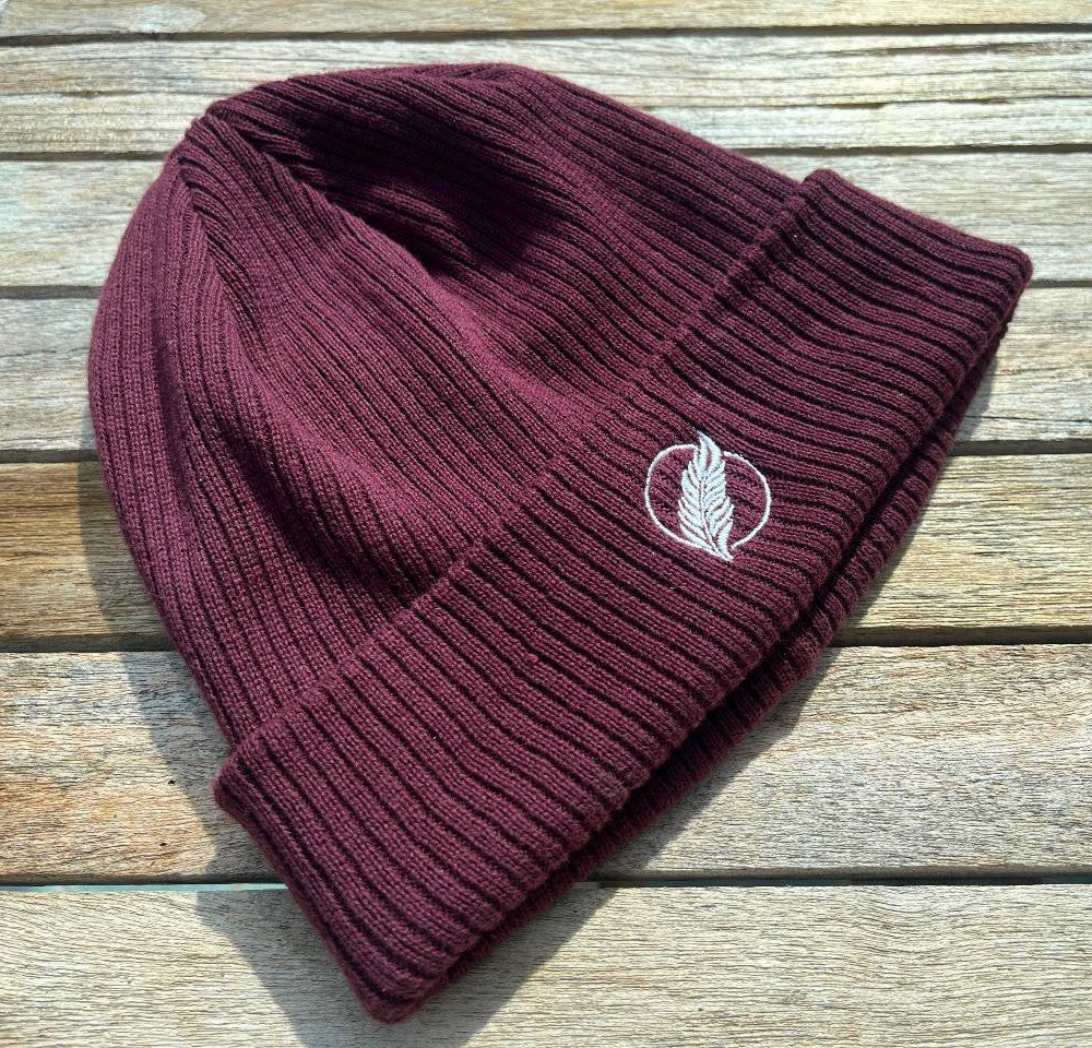 Roho Rafiki® embroidered icon organic cotton beanie. Crafted from 100% organically-sourced Control Union Certified cotton, this lightweight design in a heritage-inspired fine rib is the perfect all-year-round option for casual headwear. Embroidered with the white feather icon logo. A range of colours are available. Burgundy.