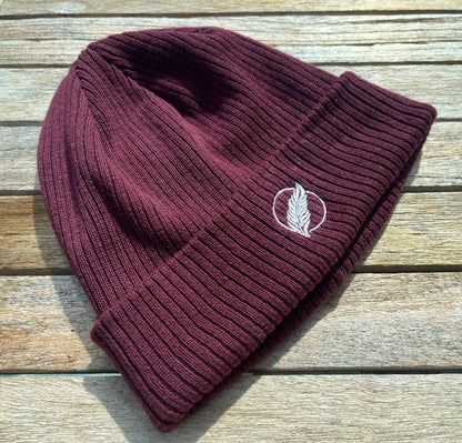 Roho Rafiki® embroidered icon organic cotton beanie. Crafted from 100% organically-sourced Control Union Certified cotton, this lightweight design in a heritage-inspired fine rib is the perfect all-year-round option for casual headwear. Embroidered with the white feather icon logo. A range of colours are available. Burgundy.